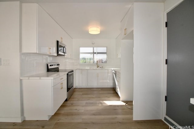 kitchen featuring decorative backsplash, light wood-type flooring, stainless steel appliances, sink, and white cabinetry