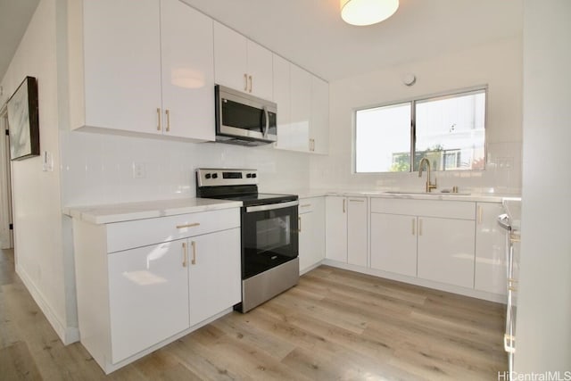 kitchen with white cabinets, appliances with stainless steel finishes, light hardwood / wood-style flooring, and sink