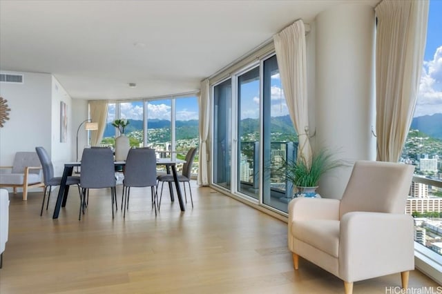 dining space featuring a wall of windows, a mountain view, and light wood-type flooring