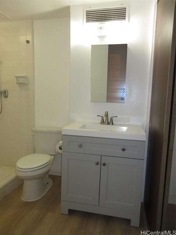 bathroom featuring toilet, hardwood / wood-style floors, vanity, and tiled shower