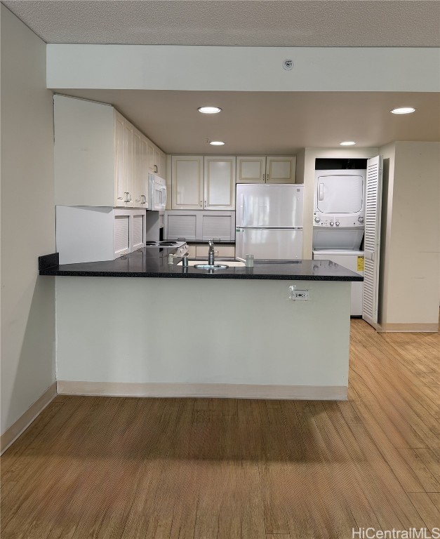 kitchen featuring light hardwood / wood-style floors, stacked washer / drying machine, stainless steel fridge, and kitchen peninsula