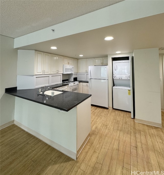 kitchen featuring kitchen peninsula, white appliances, sink, light hardwood / wood-style flooring, and stacked washer / dryer