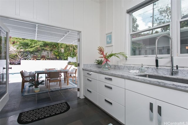 bar with white cabinetry, sink, light stone counters, and plenty of natural light