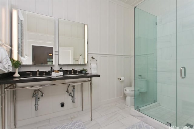 bathroom featuring toilet, a shower with door, and double sink