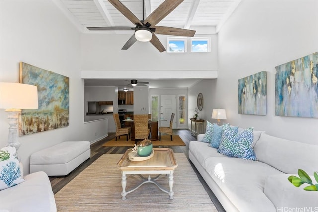 living room with wood-type flooring, a towering ceiling, ceiling fan, and beam ceiling