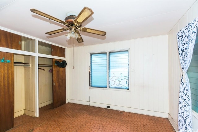 unfurnished bedroom featuring a closet, ceiling fan, and wood walls