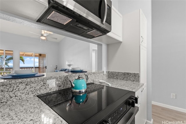 kitchen featuring black stove, light wood-type flooring, light stone counters, ceiling fan, and white cabinetry