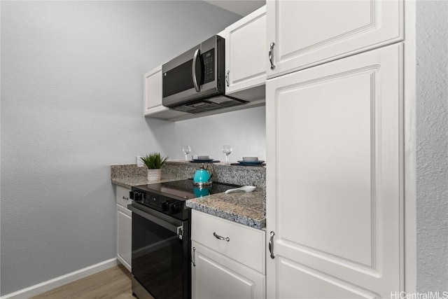 kitchen with appliances with stainless steel finishes, light wood-type flooring, white cabinetry, and dark stone countertops