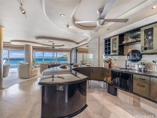 kitchen with a tray ceiling, ceiling fan, sink, and a water view