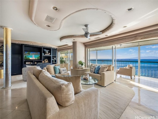 tiled living room with a raised ceiling, ceiling fan, and a water view