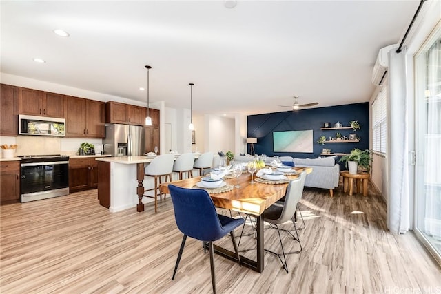 dining room featuring a wall unit AC, ceiling fan, a healthy amount of sunlight, and light wood-type flooring