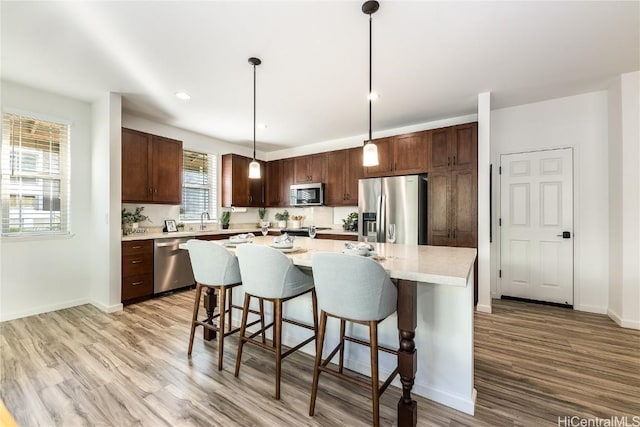 kitchen featuring sink, hanging light fixtures, light hardwood / wood-style floors, a kitchen island, and stainless steel appliances