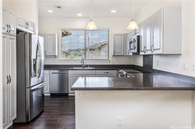 kitchen featuring sink, dark hardwood / wood-style floors, kitchen peninsula, decorative light fixtures, and appliances with stainless steel finishes