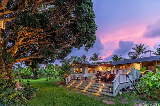 back house at dusk featuring a yard and a wooden deck