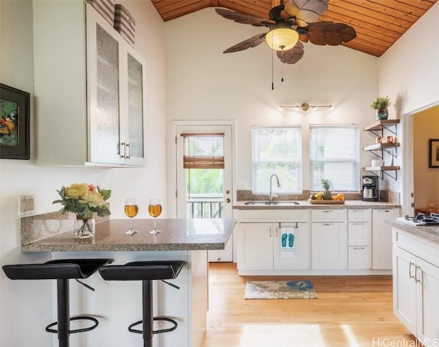 kitchen featuring wood ceiling, a breakfast bar area, light stone countertops, white cabinets, and sink