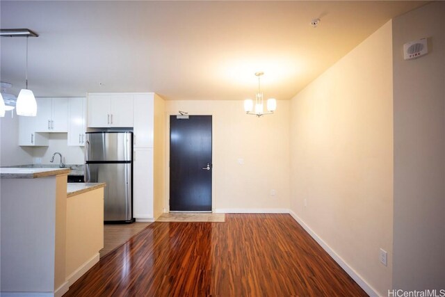 kitchen featuring dark hardwood / wood-style flooring, an inviting chandelier, white cabinets, stainless steel refrigerator, and hanging light fixtures