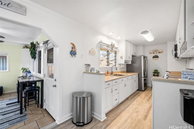 kitchen featuring light hardwood / wood-style floors, white cabinetry, sink, and stainless steel refrigerator