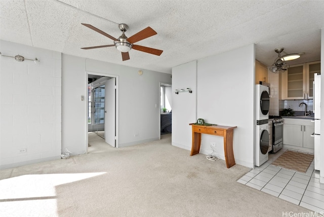 interior space featuring sink, stacked washer and dryer, ceiling fan, a textured ceiling, and light colored carpet