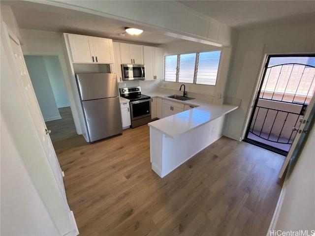 kitchen featuring wood-type flooring, sink, appliances with stainless steel finishes, white cabinetry, and kitchen peninsula