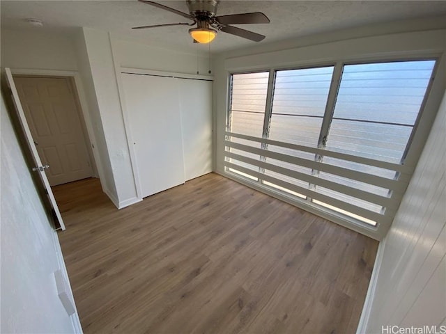 unfurnished bedroom with ceiling fan, a closet, and wood-type flooring