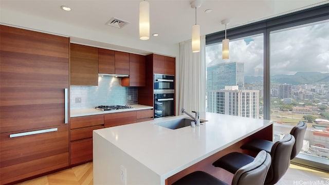 kitchen featuring a kitchen bar, backsplash, a kitchen island with sink, sink, and decorative light fixtures