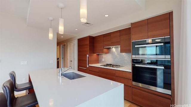 kitchen featuring a breakfast bar, sink, hanging light fixtures, and a kitchen island with sink