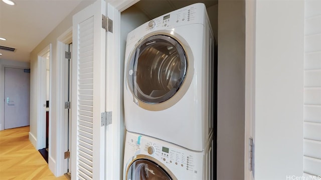 laundry room with stacked washer / drying machine and parquet floors