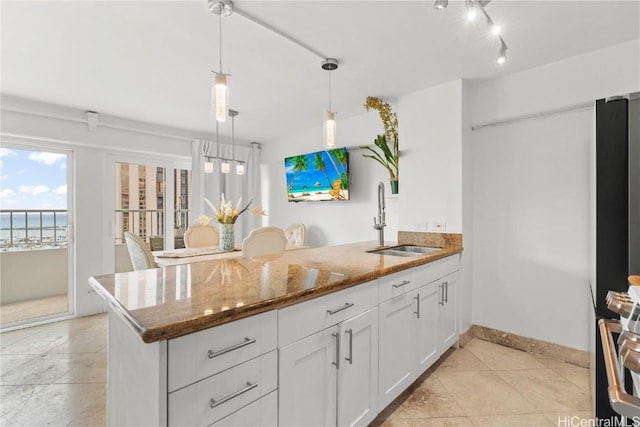 kitchen featuring stone counters, white cabinetry, hanging light fixtures, and sink