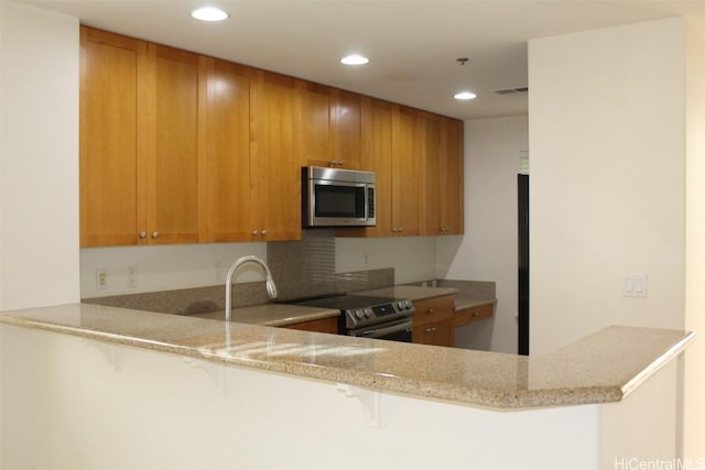 kitchen featuring kitchen peninsula, appliances with stainless steel finishes, light stone countertops, and a breakfast bar area