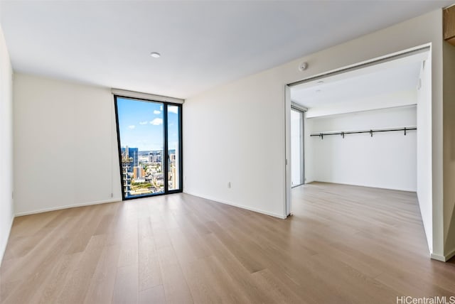 unfurnished bedroom featuring floor to ceiling windows, light hardwood / wood-style flooring, and a closet