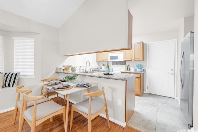 kitchen featuring kitchen peninsula, stainless steel fridge, light brown cabinetry, light stone counters, and range