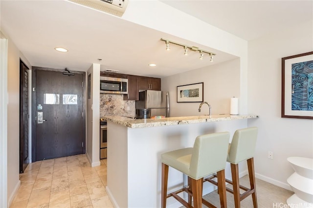 kitchen featuring a kitchen bar, dark brown cabinetry, stainless steel appliances, and kitchen peninsula