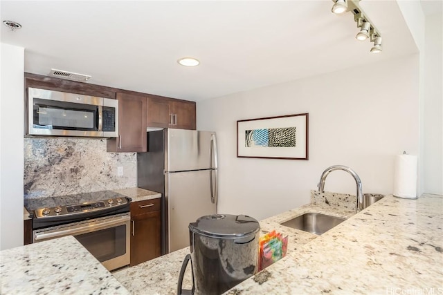 kitchen featuring light stone countertops, sink, rail lighting, decorative backsplash, and appliances with stainless steel finishes