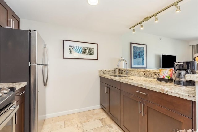 kitchen with light stone countertops, appliances with stainless steel finishes, track lighting, and sink