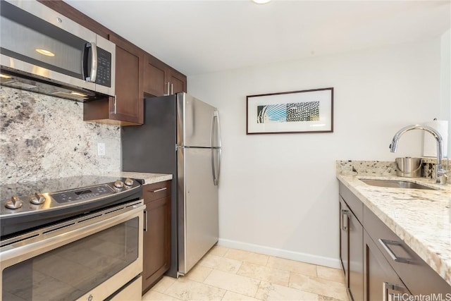 kitchen featuring sink, decorative backsplash, light stone countertops, appliances with stainless steel finishes, and dark brown cabinetry