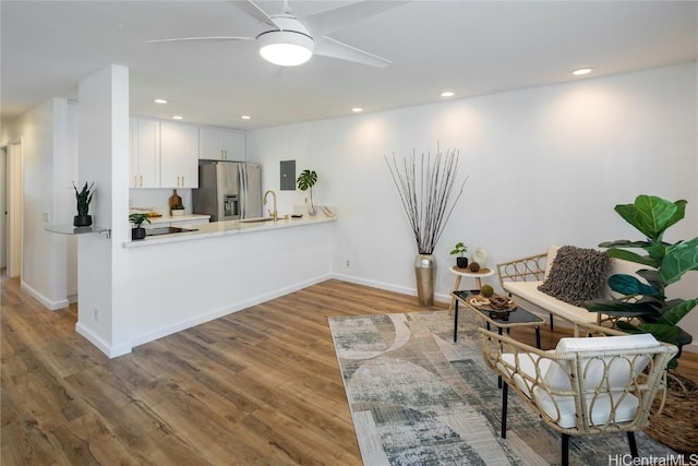 kitchen with white cabinetry, sink, kitchen peninsula, stainless steel fridge, and hardwood / wood-style floors