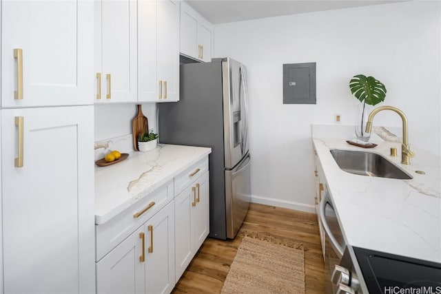 kitchen with electric panel, white cabinets, sink, light stone countertops, and light hardwood / wood-style floors