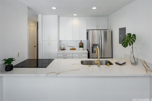 kitchen with light stone countertops, stainless steel refrigerator with ice dispenser, black electric stovetop, sink, and white cabinets