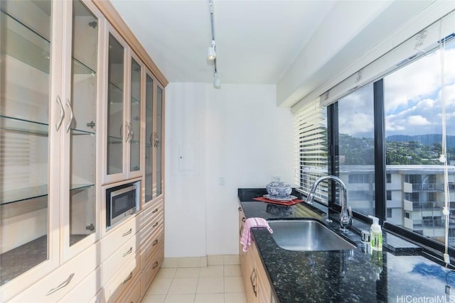 kitchen featuring pendant lighting, track lighting, sink, dark stone countertops, and light tile patterned floors