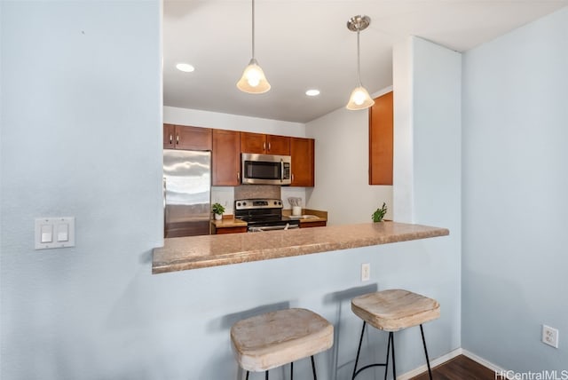 kitchen featuring kitchen peninsula, appliances with stainless steel finishes, backsplash, a breakfast bar, and pendant lighting