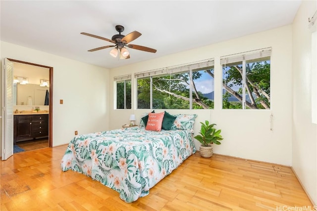 bedroom with light wood-type flooring, connected bathroom, multiple windows, and ceiling fan