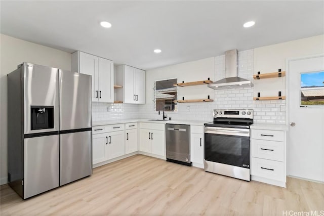 kitchen with white cabinets, stainless steel appliances, wall chimney exhaust hood, and light hardwood / wood-style floors