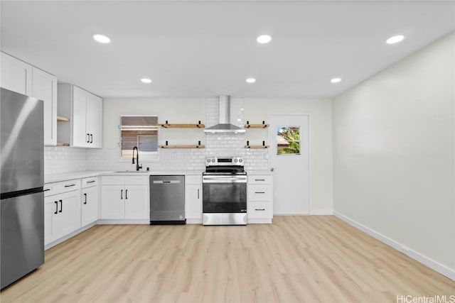 kitchen featuring white cabinets, light wood-type flooring, stainless steel appliances, and wall chimney range hood