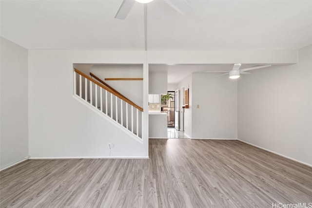 unfurnished living room featuring ceiling fan, stairway, wood finished floors, and baseboards