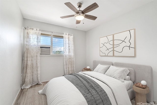 bedroom featuring a ceiling fan, baseboards, cooling unit, and wood finished floors