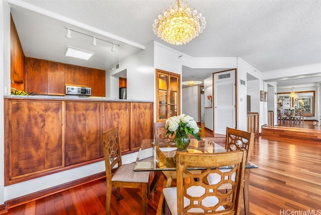 dining area with rail lighting, crown molding, hardwood / wood-style floors, a chandelier, and a textured ceiling