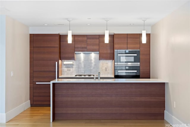 kitchen featuring decorative backsplash, decorative light fixtures, light hardwood / wood-style flooring, and stainless steel appliances