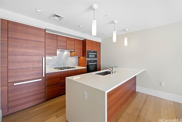 kitchen featuring sink, an island with sink, pendant lighting, stainless steel gas stovetop, and light wood-type flooring