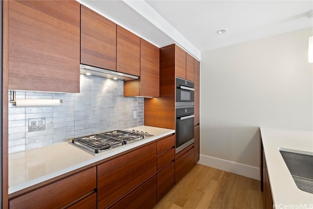 kitchen with stainless steel gas cooktop, ventilation hood, light hardwood / wood-style floors, decorative backsplash, and double wall oven