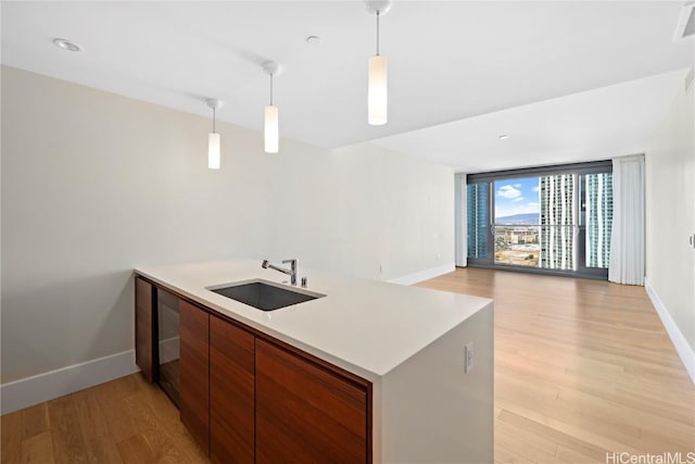 kitchen featuring kitchen peninsula, light wood-type flooring, decorative light fixtures, and sink